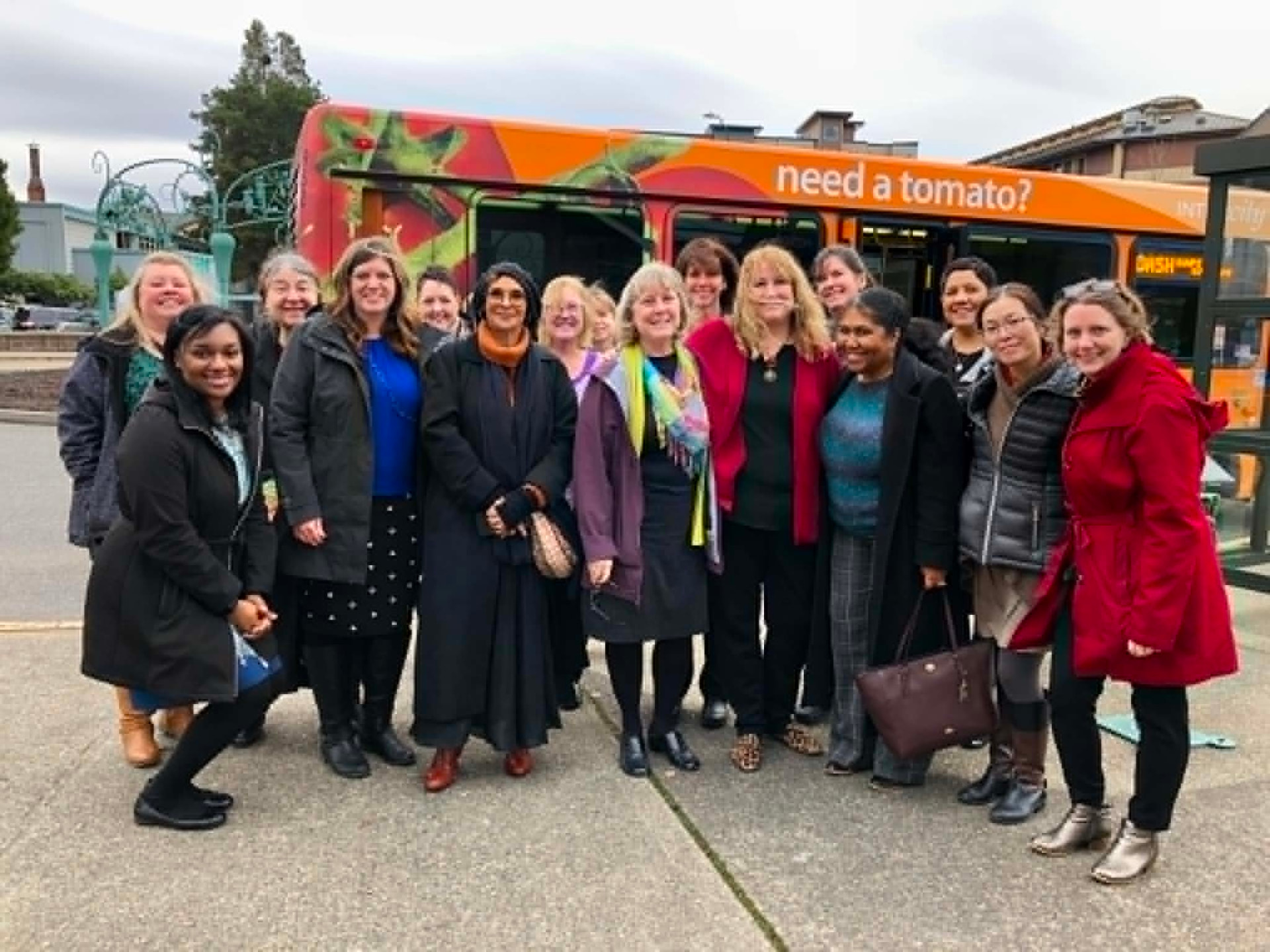 An Academy cohort gathered outside in front of a transit bus during a site visit